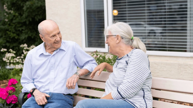 Two seniors talking on a bench outside a retirement home