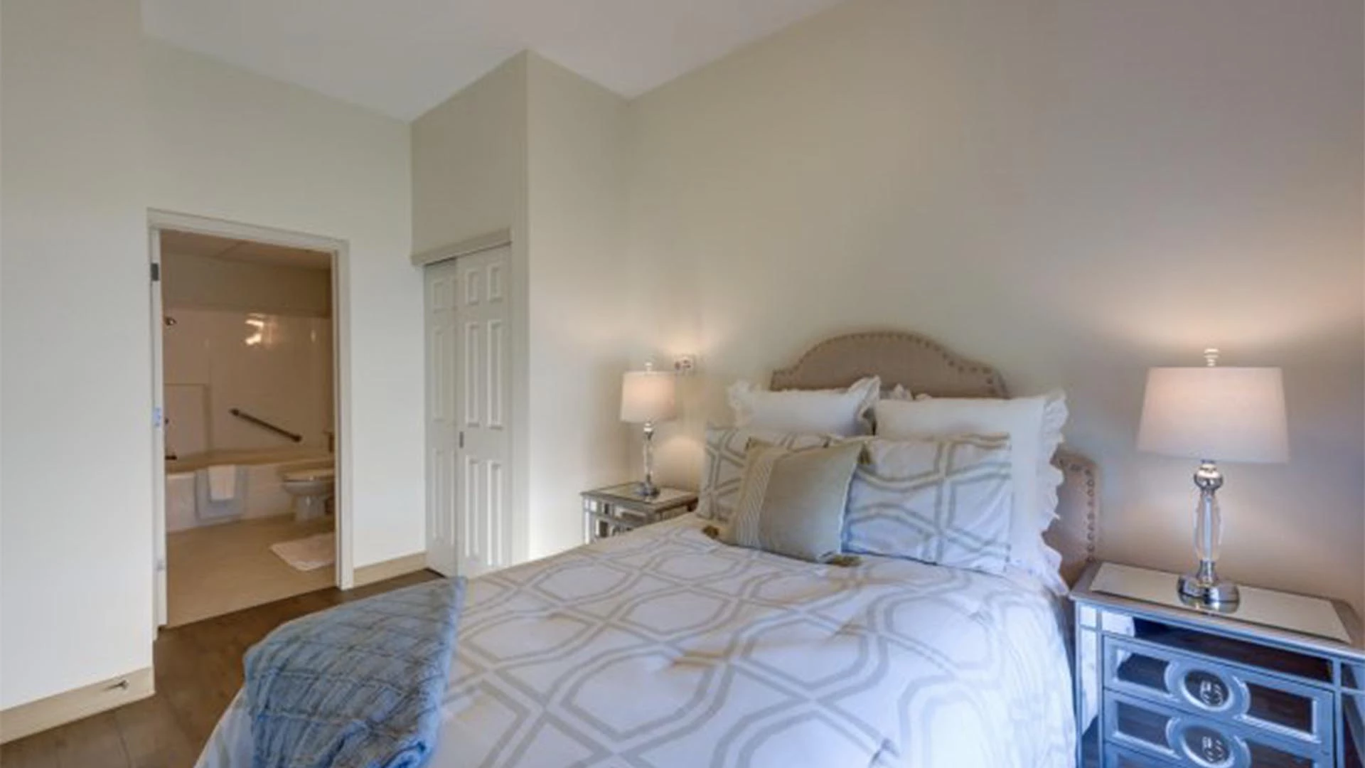 A bedroom with nightstands and bed and view of a bathroom at Rutherford Heights senior apartments